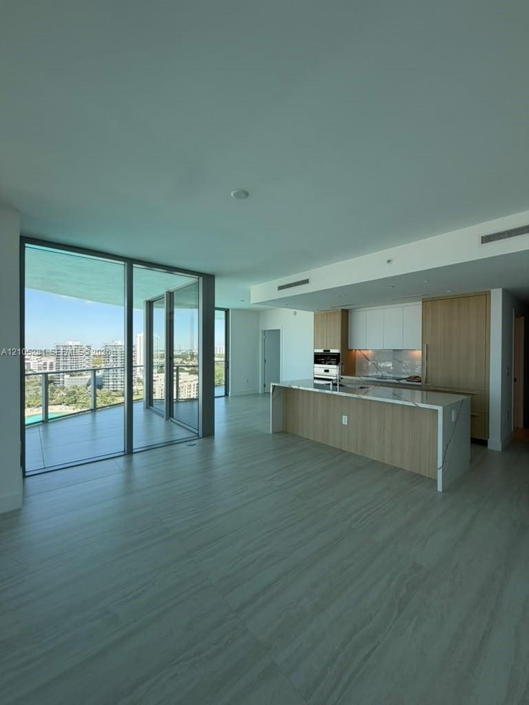 Open-concept kitchen featuring two-toned cabinetry, stone-surfaced waterfall island, and built-in appliances, accented by large floor-to-ceiling glass