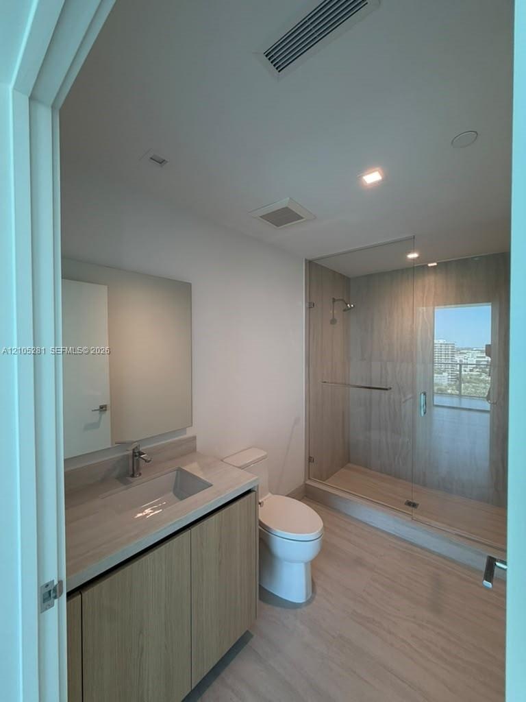 Bathroom featuring a floating vanity with a light wood-finish cabinet, integrated countertop and sink, glass-enclosed walk-in shower with large-format