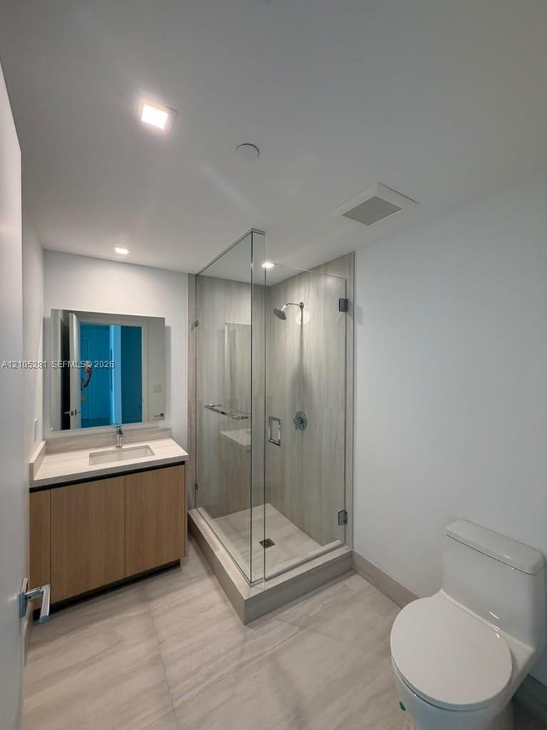 Bathroom featuring a wood-finish vanity with a stone countertop, an integrated rectangular sink, a glass-enclosed shower with large-format wall tile, 