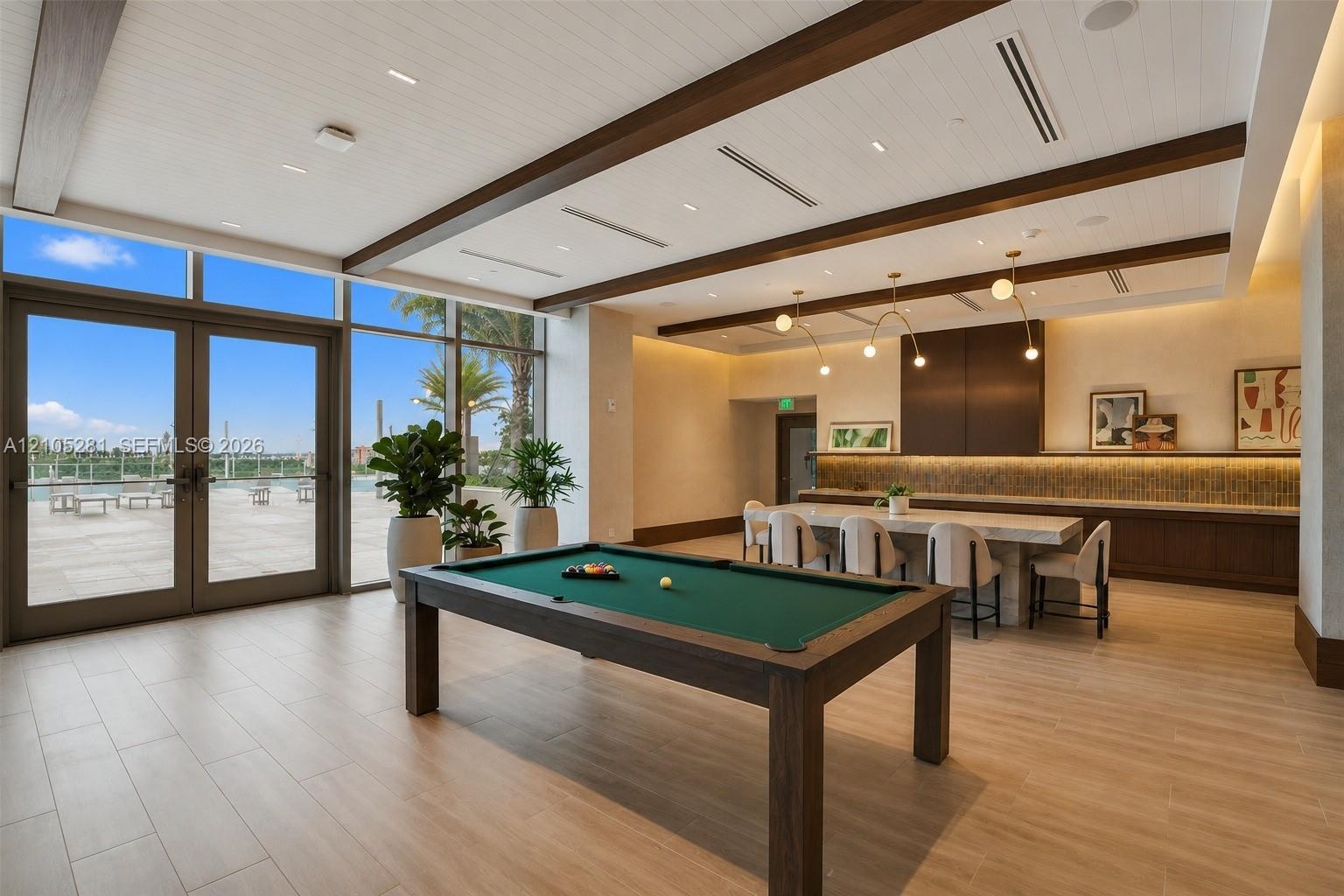 Expansive interior space featuring plank-style tile flooring, exposed wood-beam ceiling, built-in cabinetry with tiled backsplash, and floor-to-ceilin