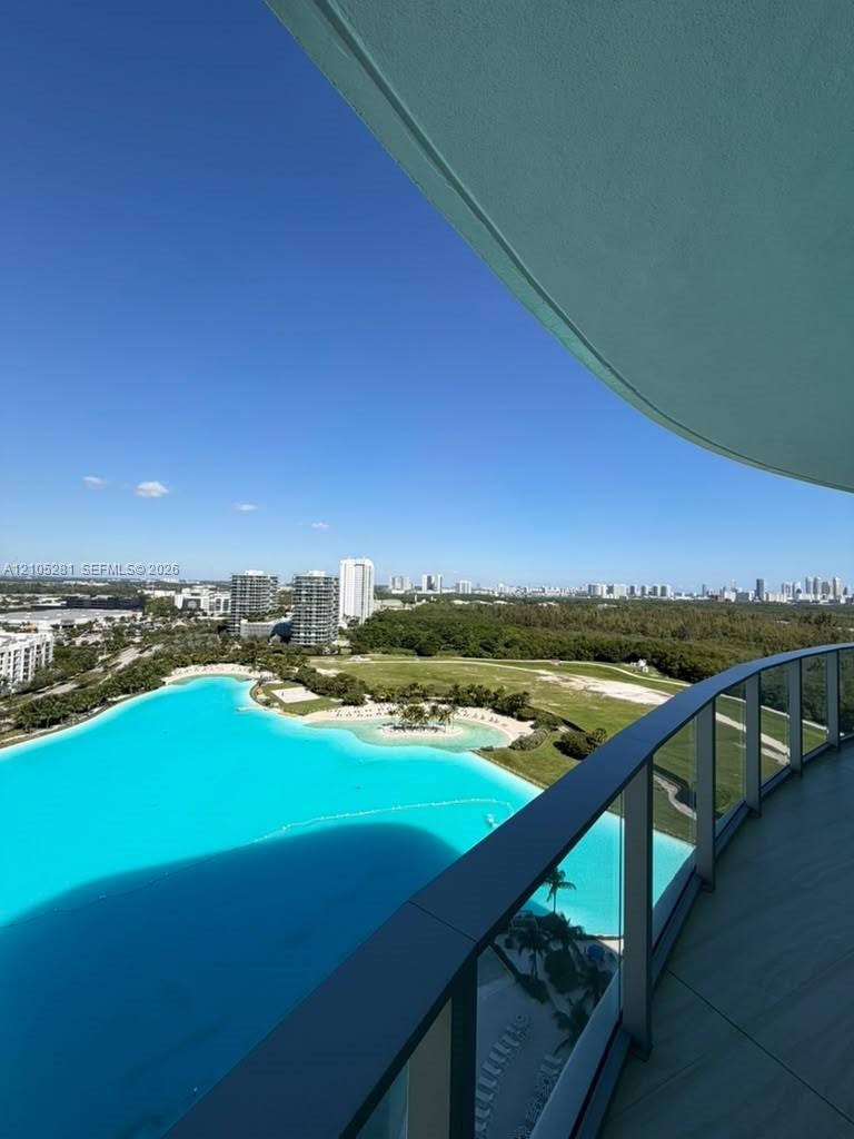 Curved balcony with glass railing, large-format tile flooring, and panoramic scenery of a turquoise lagoon and surrounding landscape