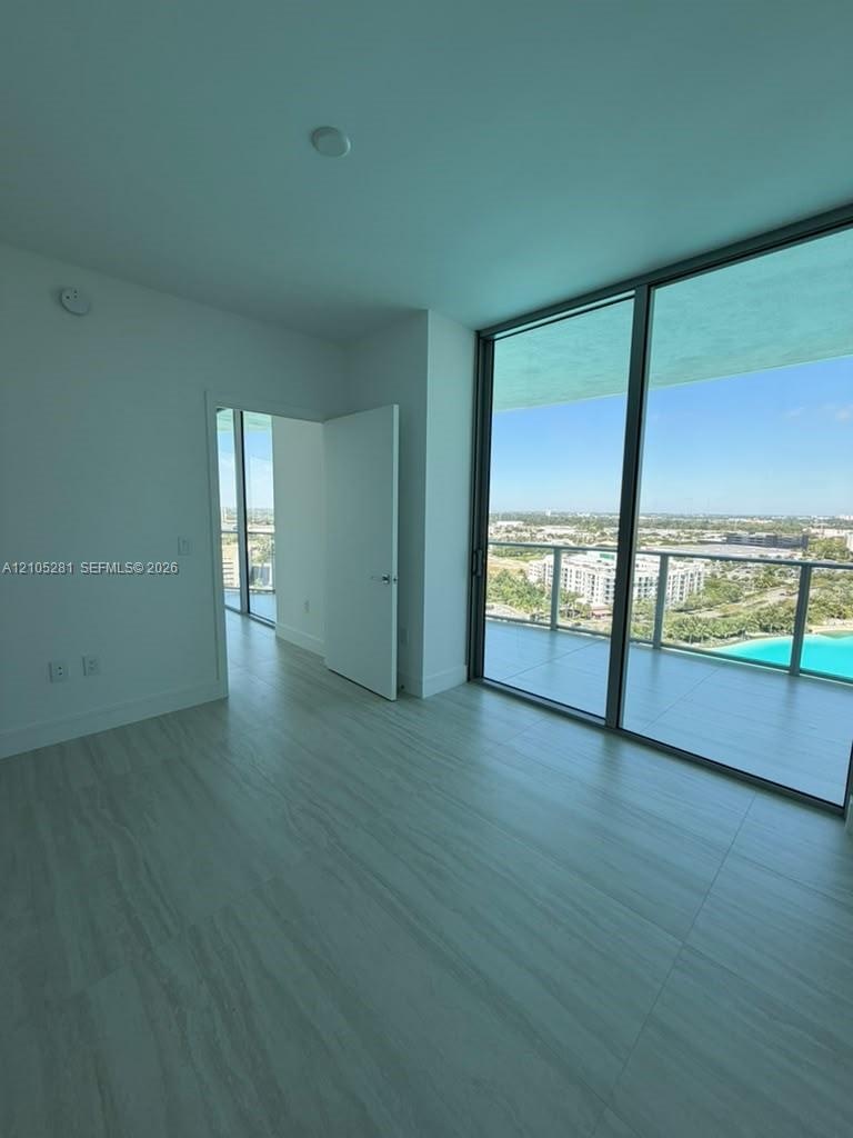 Floor-to-ceiling glass windows, neutral tile flooring, and a private balcony featuring a glass railing