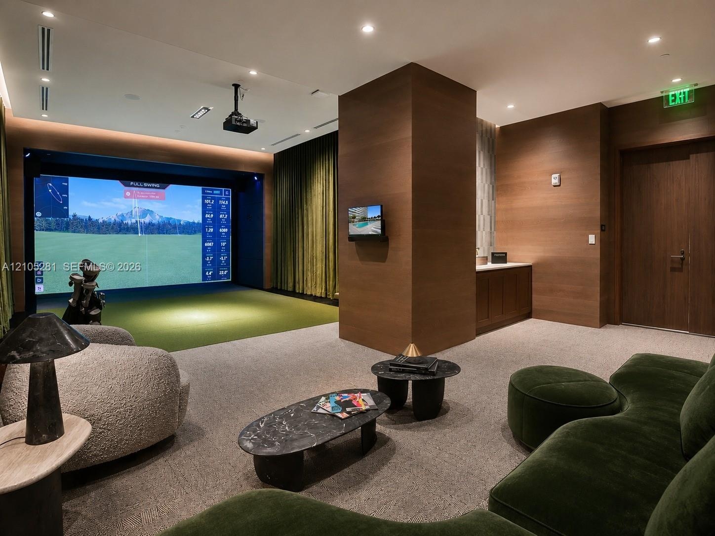 Indoor golf simulator room featuring integrated ceiling lighting, wood-paneled walls, built-in cabinetry, and wall-mounted projection equipment
