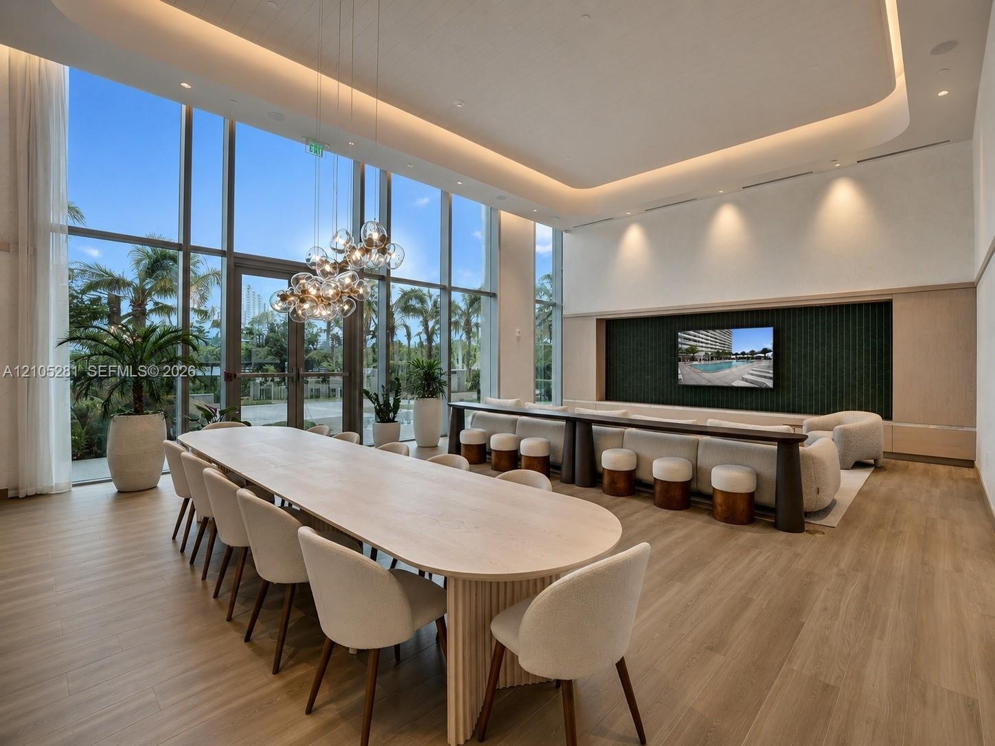 Double-height floor-to-ceiling windows, wood-finish flooring, recessed tray ceiling with integrated lighting, custom fluted millwork, and a textured w