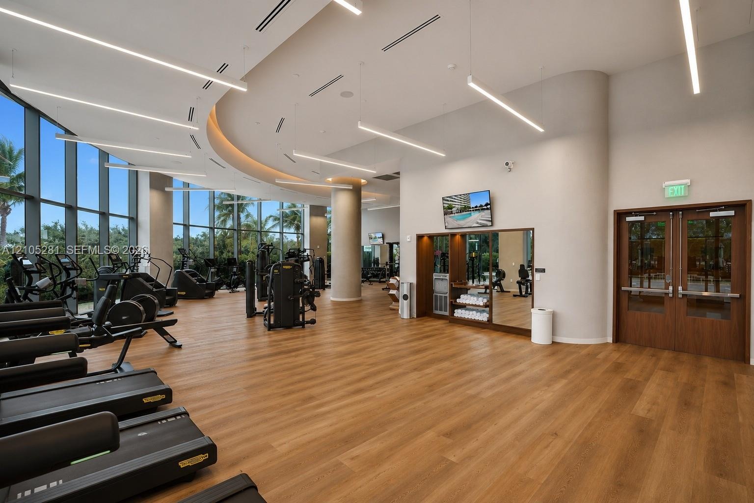 Fitness facility featuring floor-to-ceiling windows, wood-finish flooring, recessed architectural cove lighting, and suspended linear light fixtures