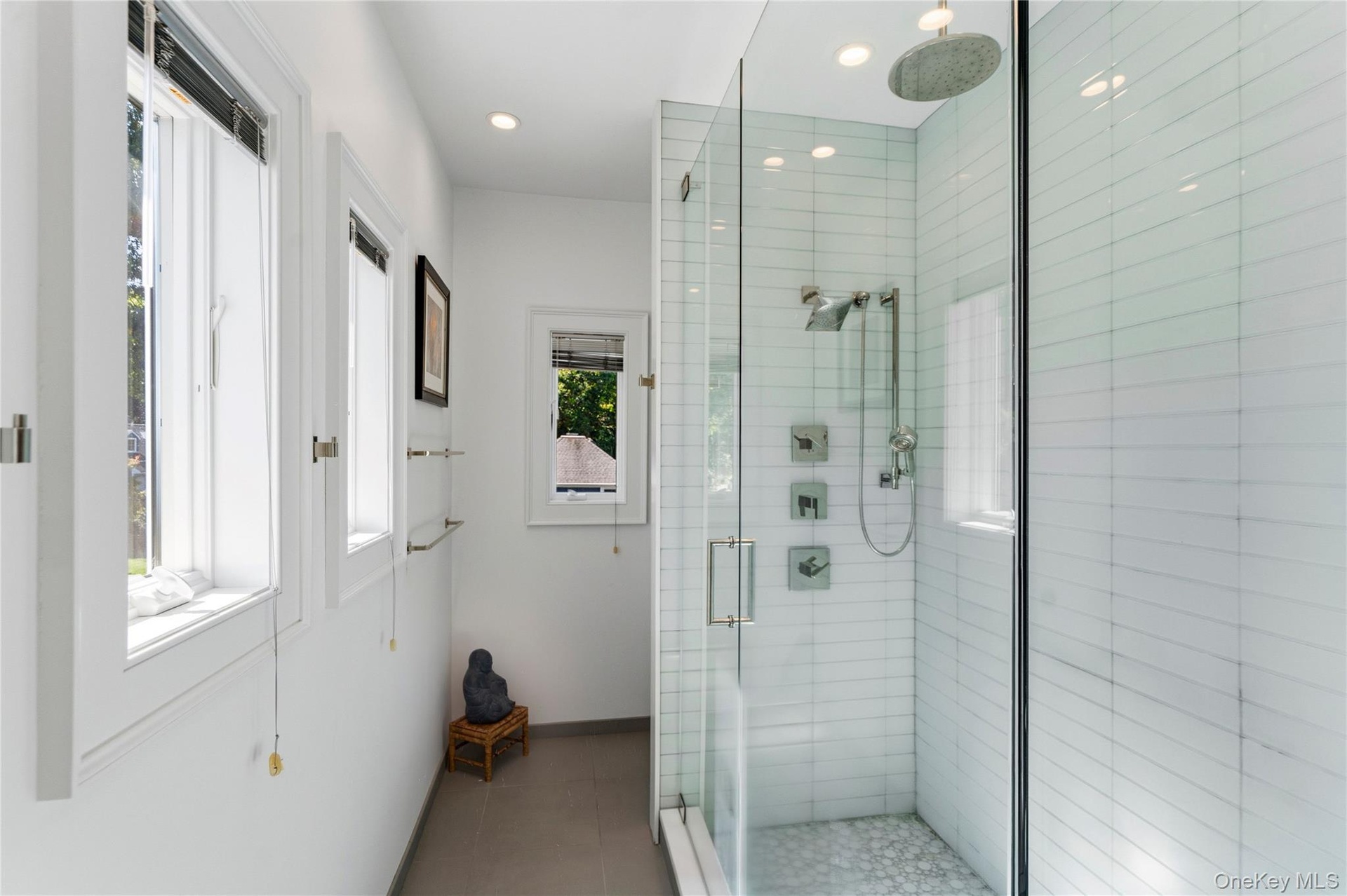 Walk-in shower featuring glass paneling, white subway tile surround, rainfall showerhead, handheld shower sprayer, and stone tile flooring