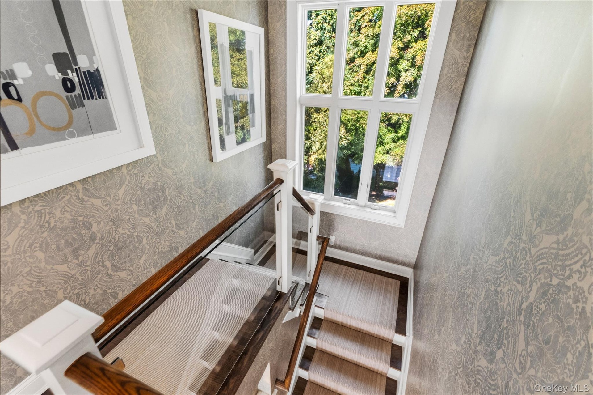 Staircase featuring glass panel railings, wood handrails, patterned wall covering, and a multi-pane window