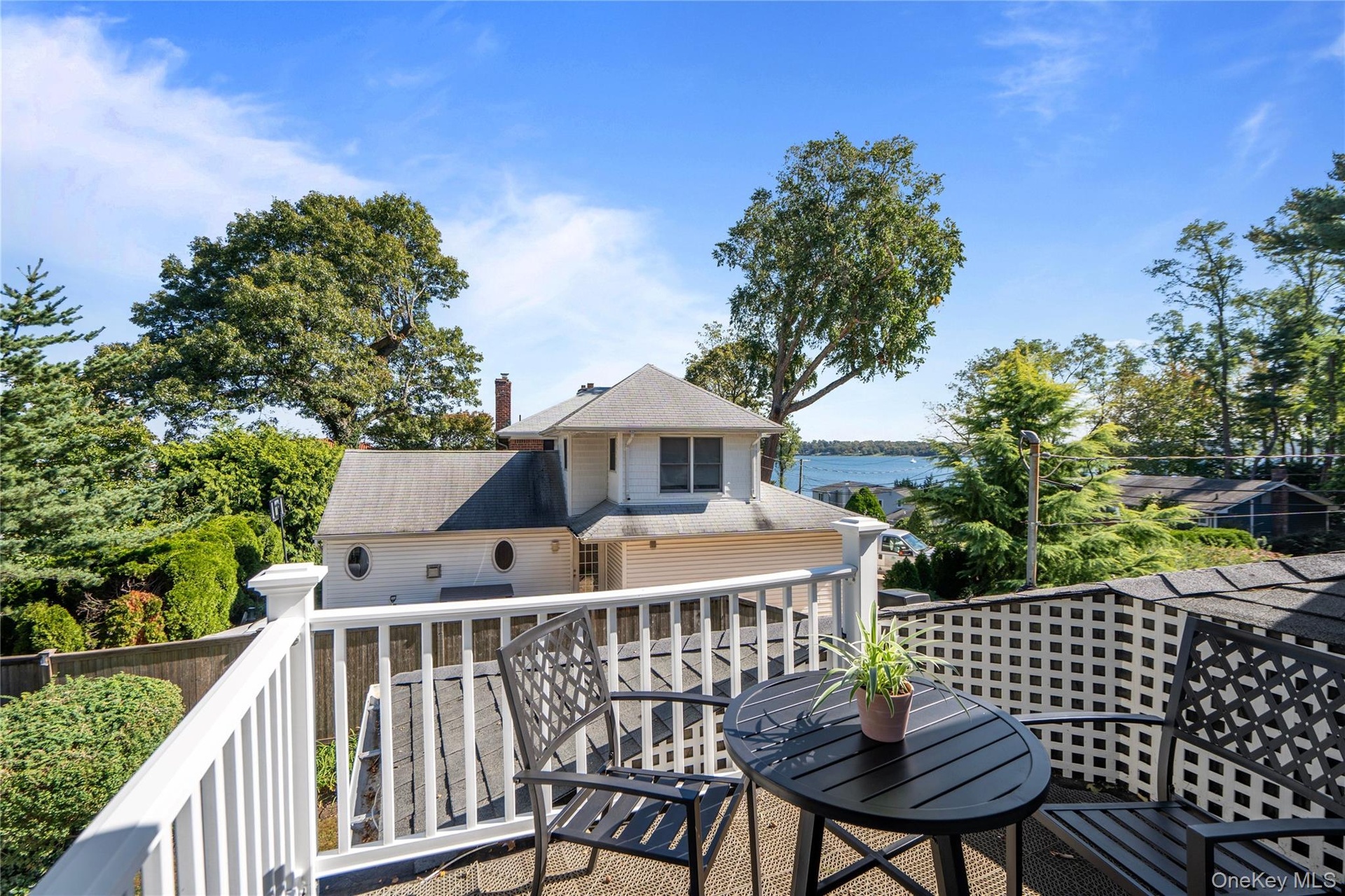 Elevated deck featuring white railing and lattice screen, overlooking mature trees and coastal scenery