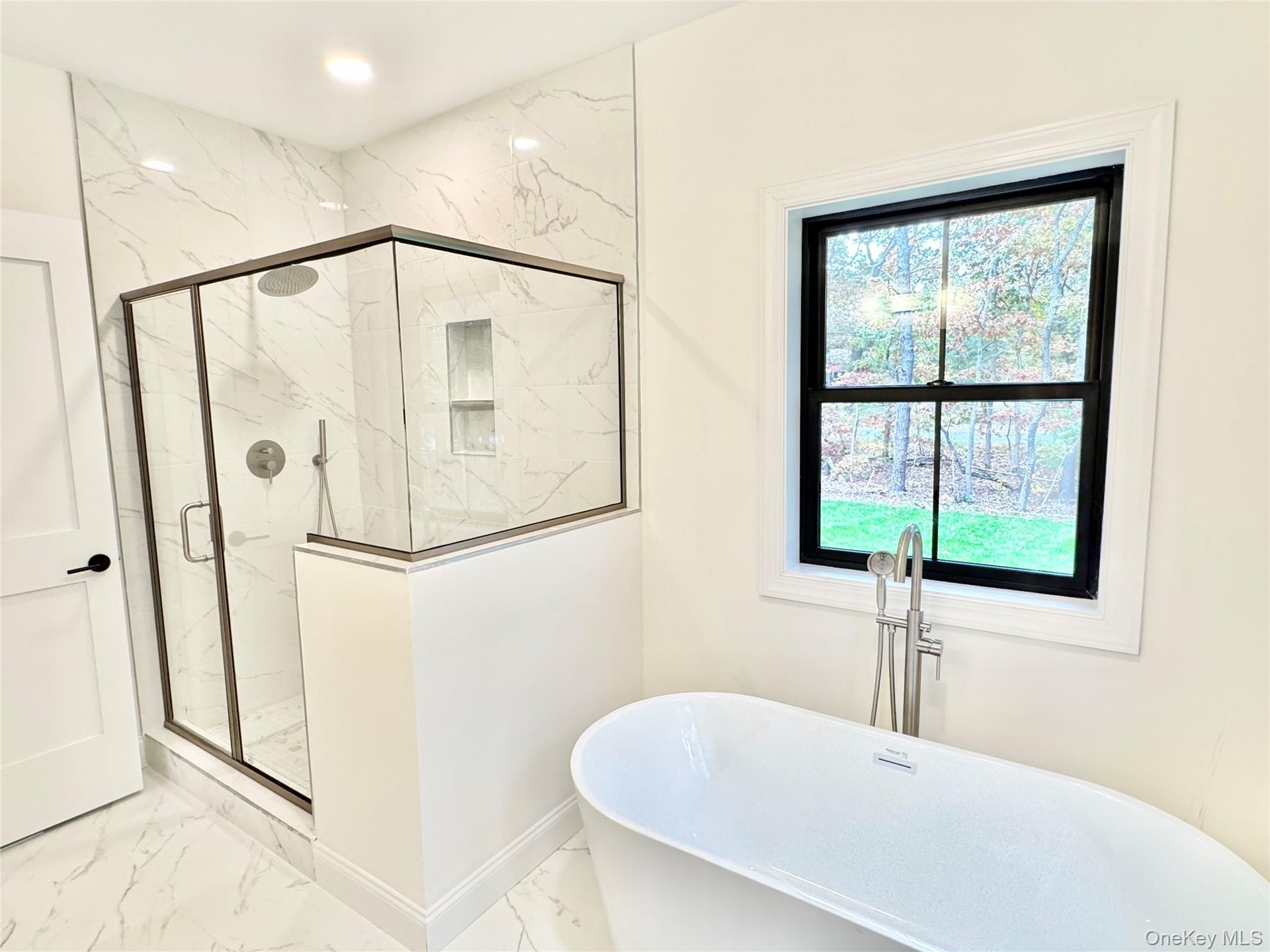 Full bath featuring marble finish floors, a freestanding bath, and a marble finish shower