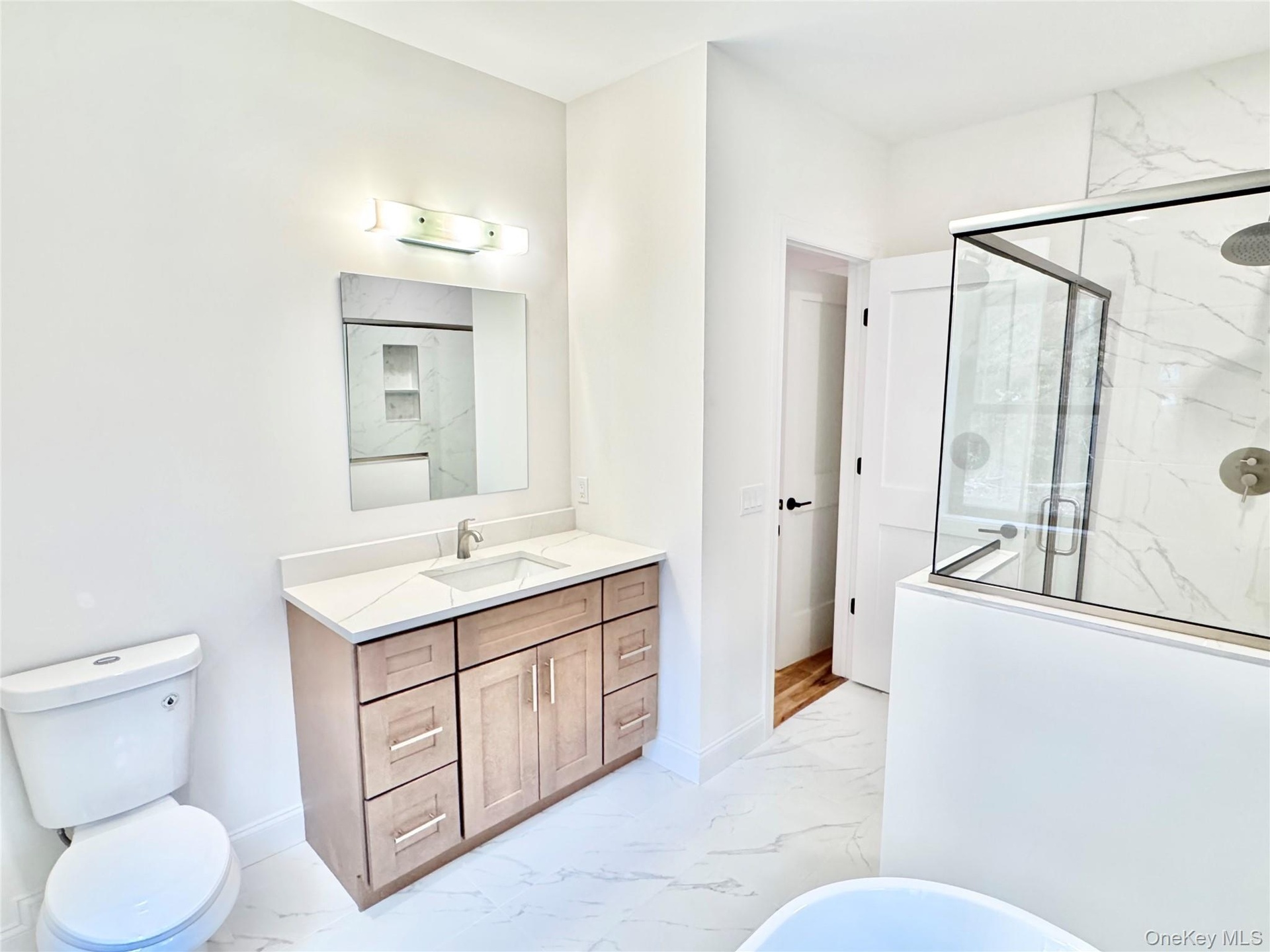 Bathroom featuring light marble finish flooring, a marble finish shower, vanity, and a freestanding tub