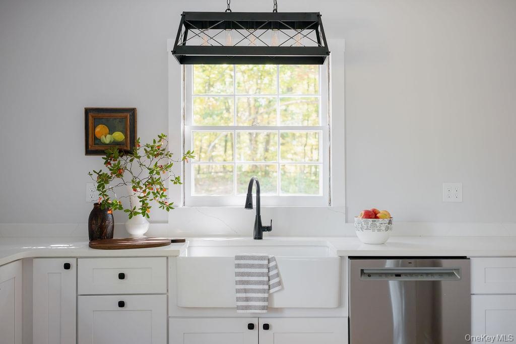 Farmhouse-style apron front sink with a matte black high-arc faucet, white shaker-style cabinetry, solid surface countertops, stainless steel dishwash