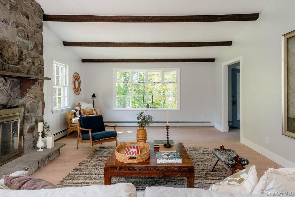 Living area featuring exposed wooden ceiling beams, floor-to-ceiling natural stone fireplace, wood-finish flooring, and multi-pane window