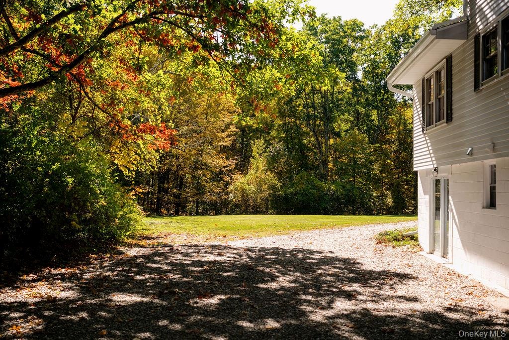 Exterior siding, gravel driveway, and expansive lawn bordered by mature trees