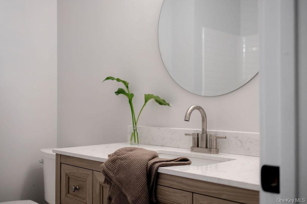 Bathroom vanity featuring a wood-finish cabinet, stone-patterned countertop with an integrated basin, brushed-nickel faucet, and a circular wall-mount