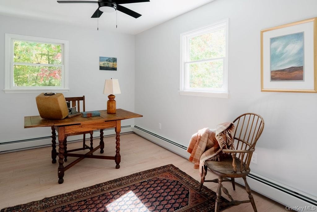 Room featuring wood-finish flooring, dual windows with exterior greenery, and a ceiling-mounted light fixture with a fan