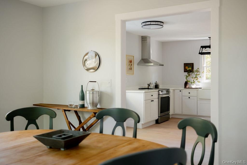 Kitchen featuring white shaker-style cabinetry, stainless steel range with a wall-mounted chimney hood, farmhouse-style sink, and flush-mount ceiling 