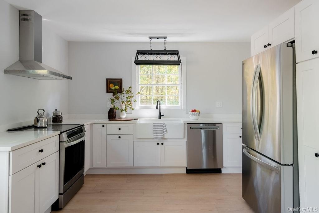 Kitchen featuring white Shaker-style cabinetry, stainless steel appliances, a farmhouse sink with a matte black faucet, wood-finish flooring, and a co