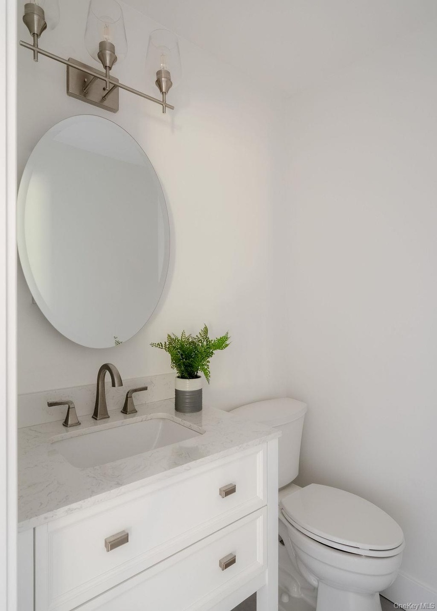 White vanity with stone-composite countertop, undermount sink, brushed nickel widespread faucet, oval mirror, and three-light wall-mounted fixture