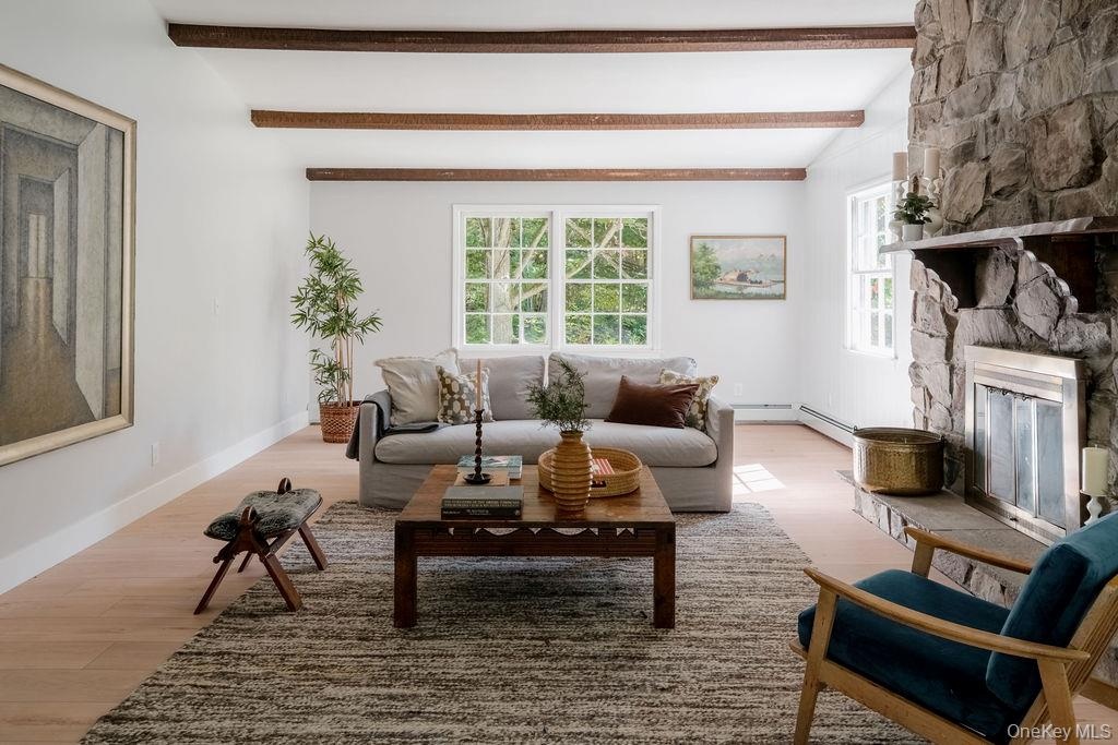 Living area featuring wood-finish flooring, exposed ceiling beams, and a floor-to-ceiling stone fireplace with a stone hearth