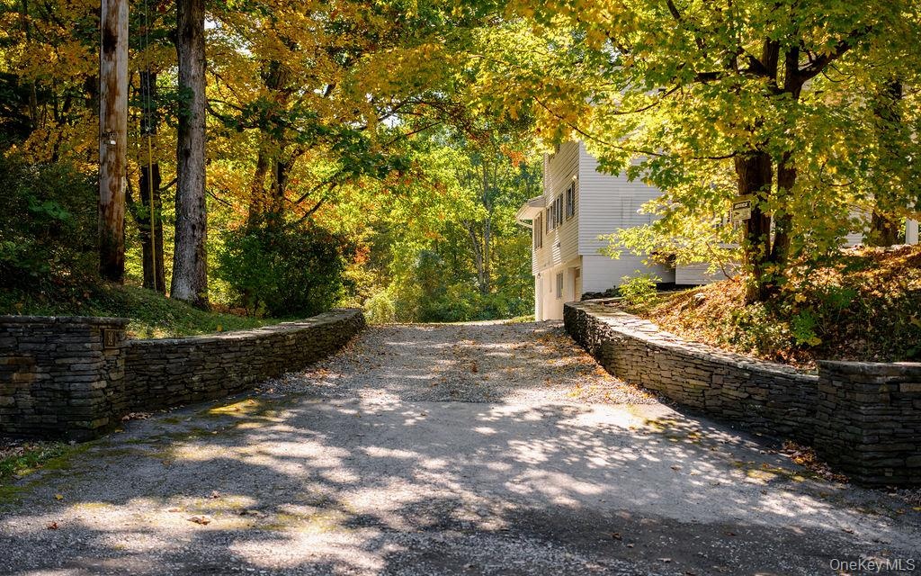 Paved driveway framed by stone retaining walls and mature trees