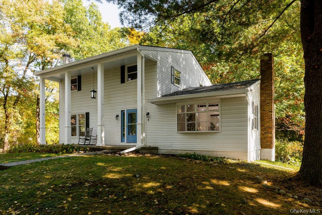 Two-story colonial-style exterior featuring white horizontal siding, a covered front porch with columns, a prominent brick chimney, and a multi-pane b