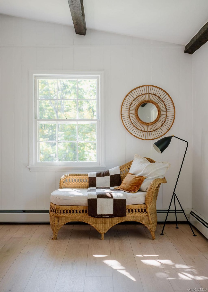 Vertical wood-paneled walls, exposed ceiling beams, light-tone wood-finish flooring, and a single-hung window with a grid pattern