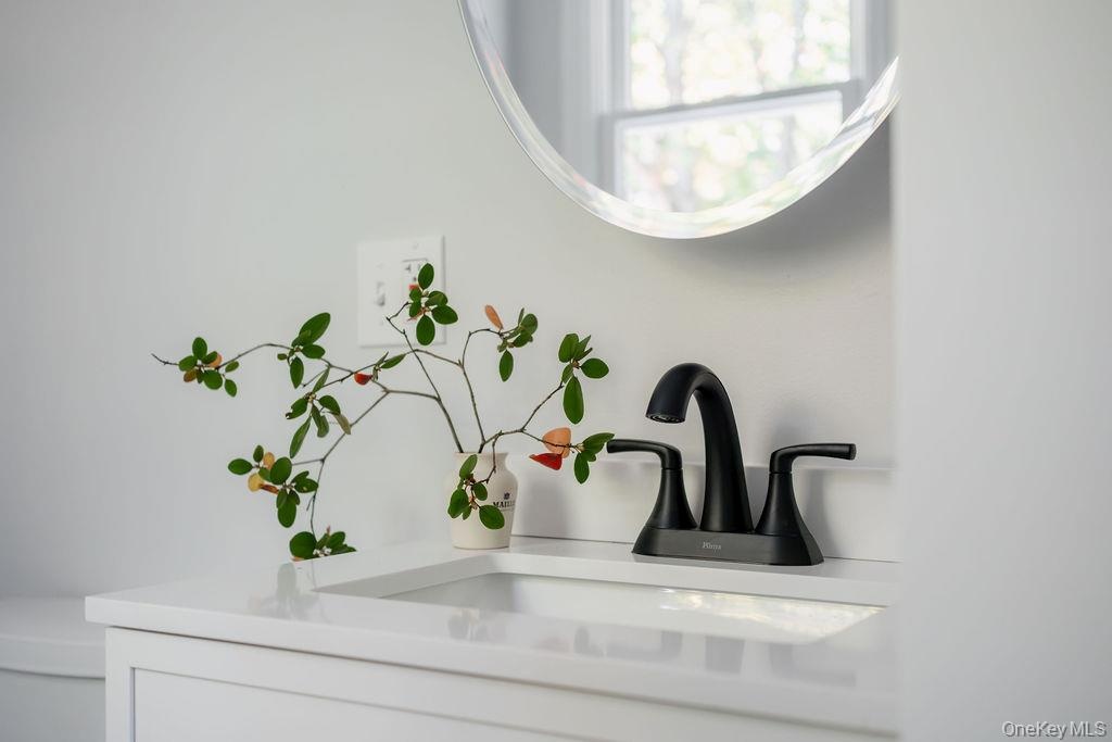 White vanity featuring a rectangular integrated sink, white countertop, matte black dual-handle faucet, and circular wall-mounted mirror