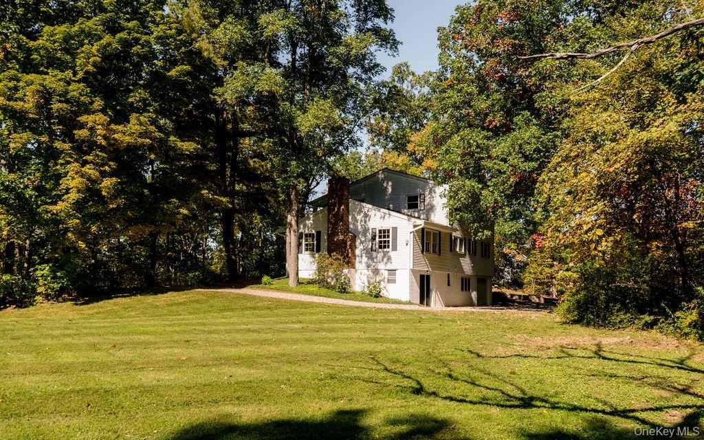 Multi-level exterior with light-colored siding, brick chimney, shuttered windows, and a generous lawn surrounded by mature trees