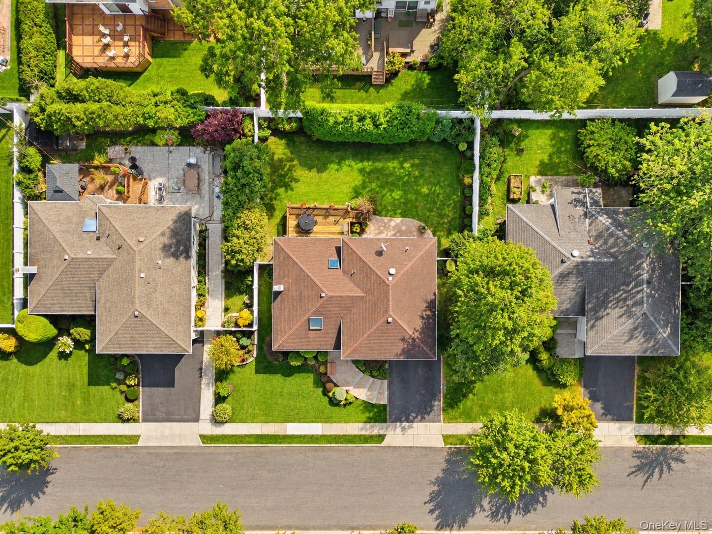 Aerial perspective of the property featuring a rear wood deck, manicured lawn, established landscaping, and a fenced perimeter