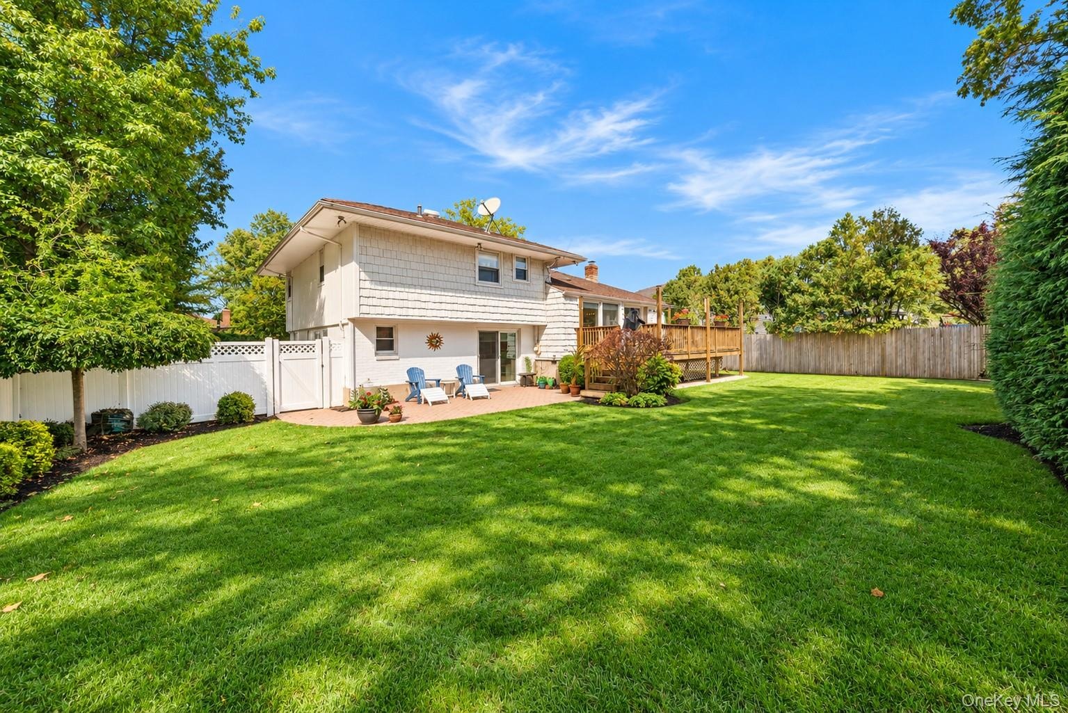 Expansive backyard featuring a large grass lawn, a paved stone patio, an elevated wooden deck, and perimeter privacy fencing