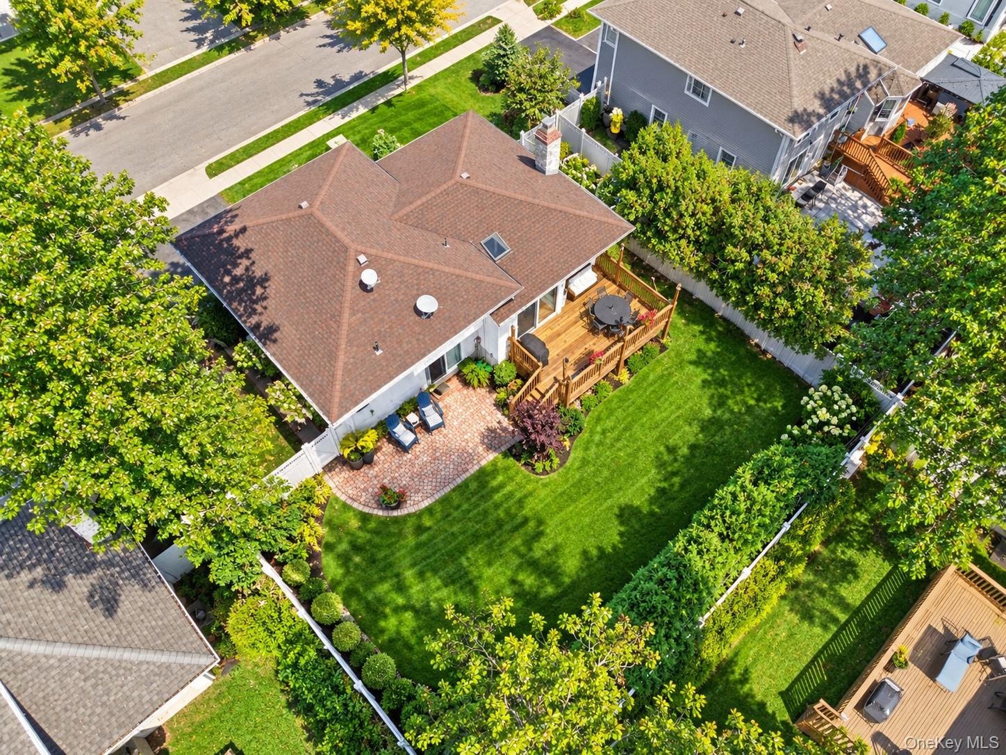 Backyard featuring an elevated wood deck, a brick patio, a manicured lawn, perimeter fencing, and mature trees