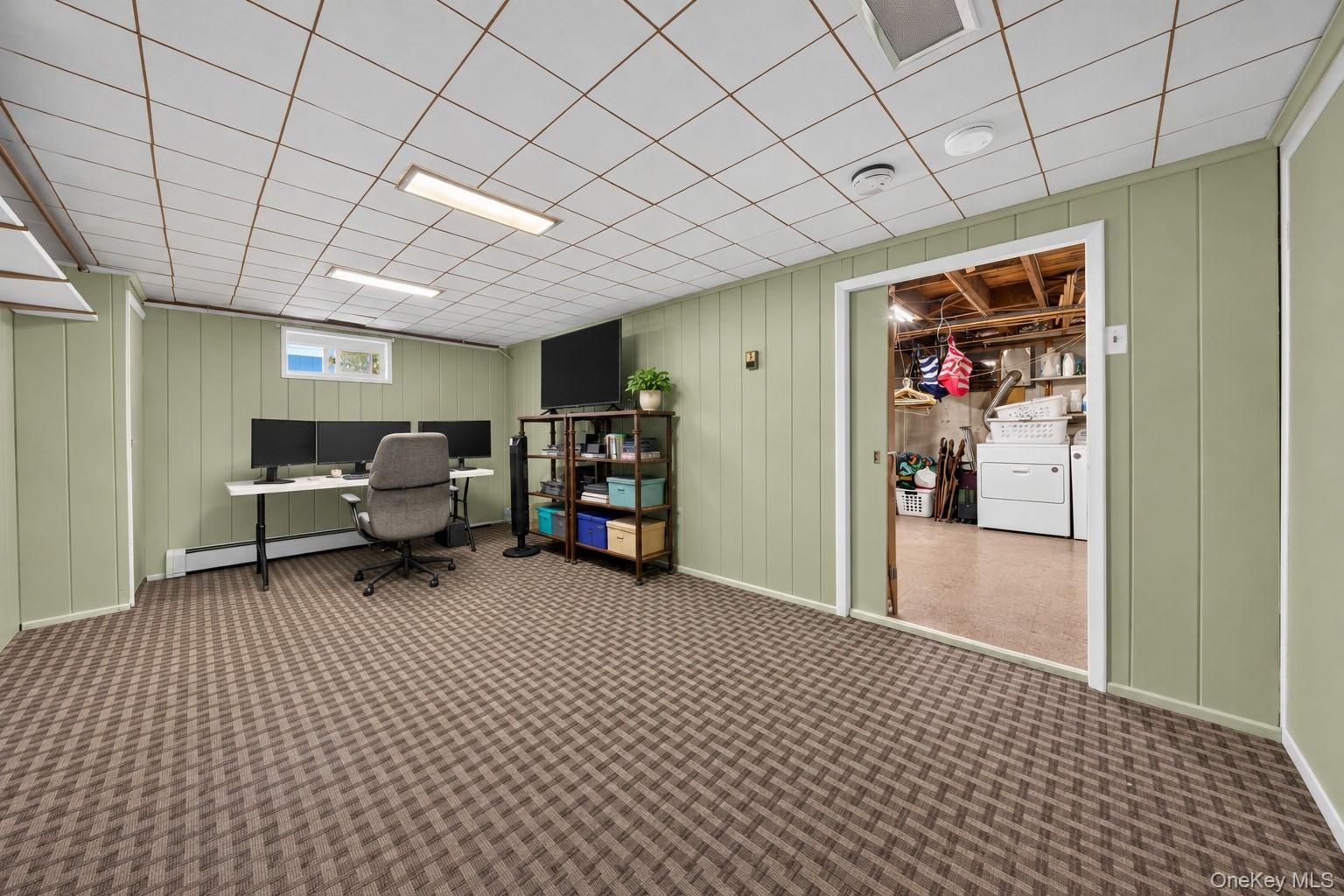 Finished interior space featuring patterned wall-to-wall carpeting, paneled walls, a drop ceiling with recessed lighting, and a sliding door entry