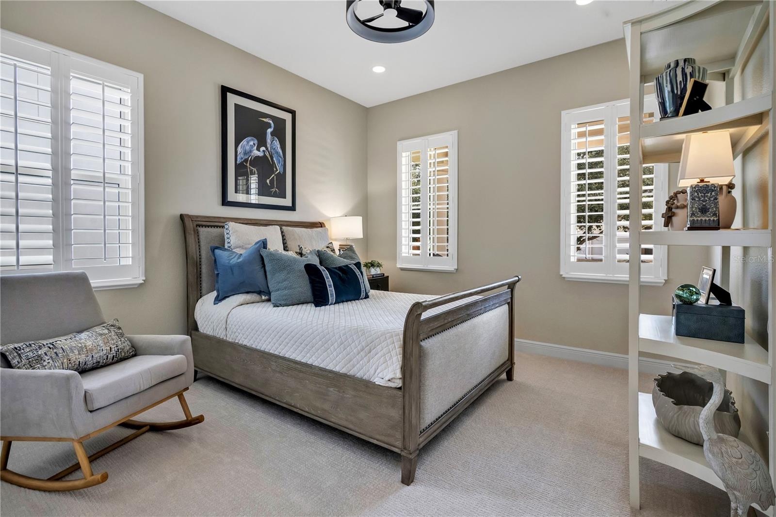 Inviting bedroom with plantation shutters and natural light from multiple windows.