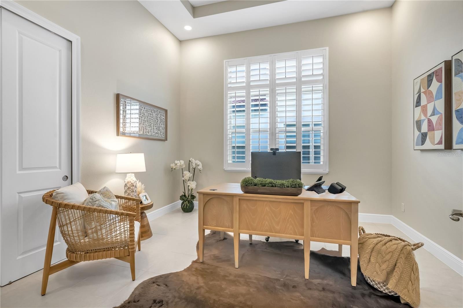 Dedicated home office featuring a tray ceiling, plantation shutters, and natural light.