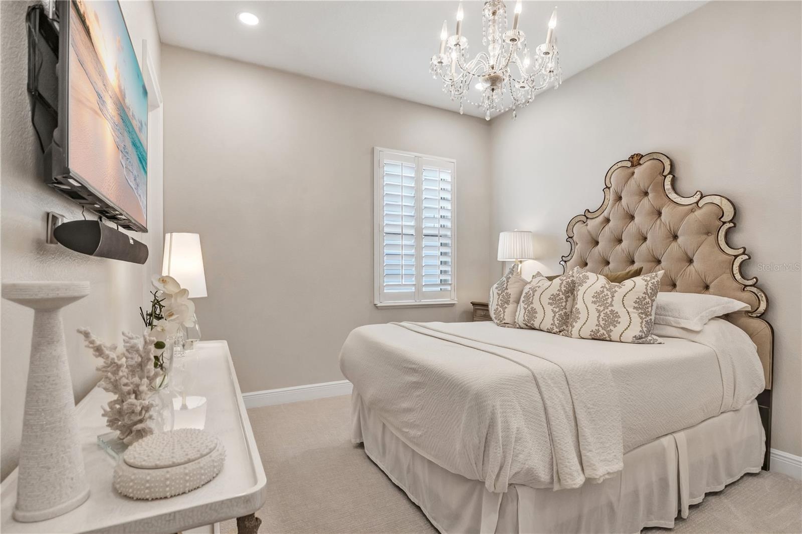 Beautifully appointed bedroom featuring a crystal-style chandelier and plantation shutters.