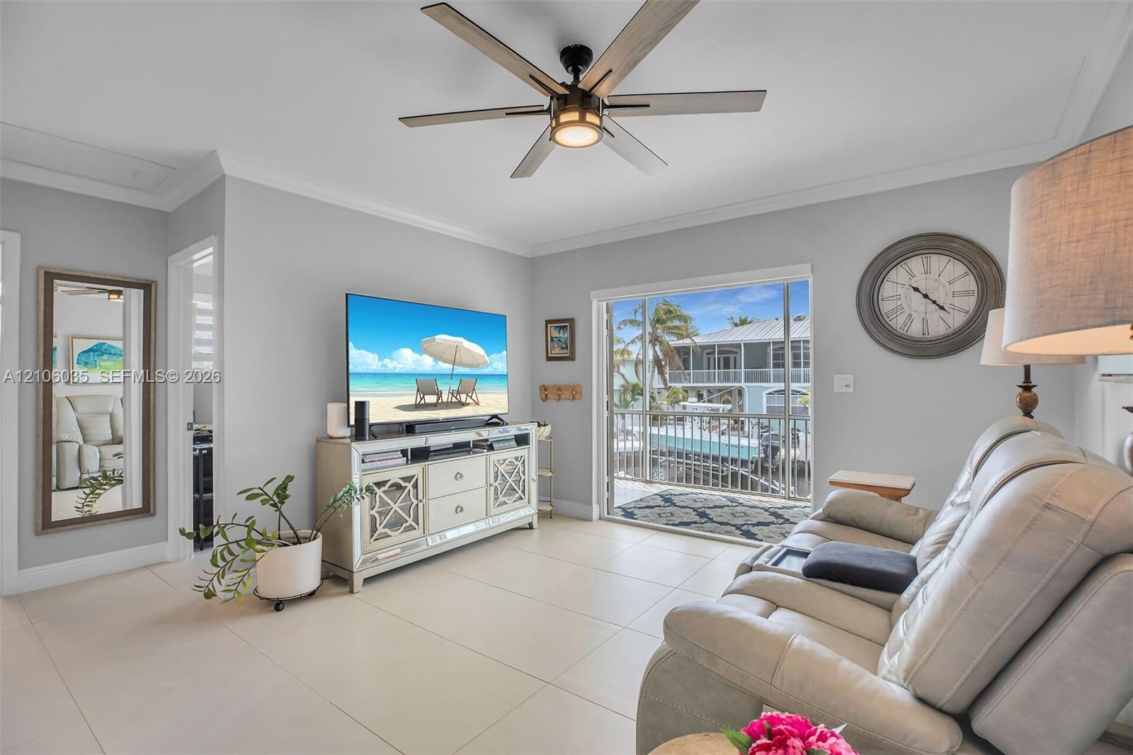Living area featuring large-format tile flooring, a multi-blade ceiling fan with integrated lighting, crown molding, and sliding glass doors opening t