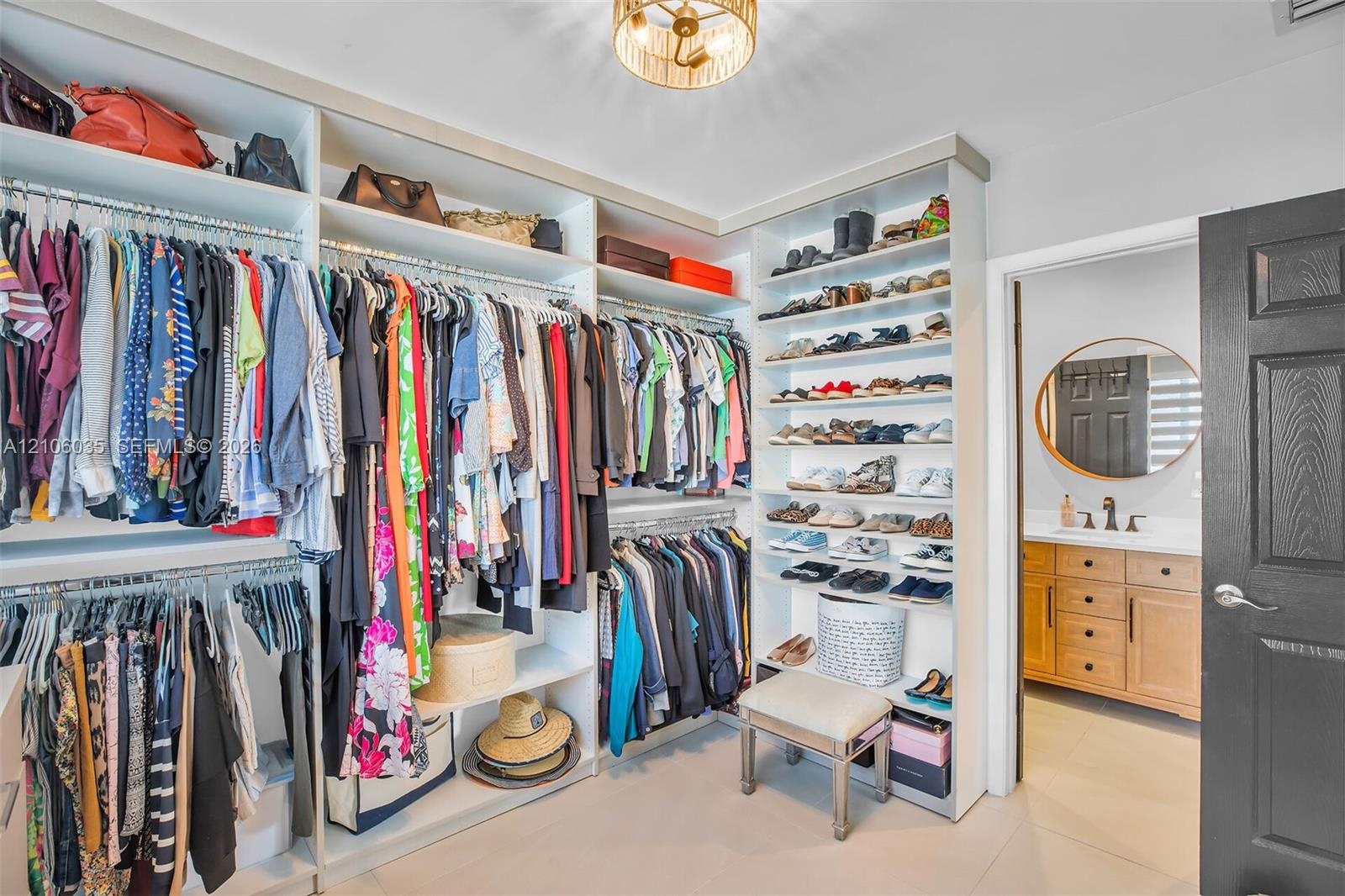 Custom built-in closet organization system with floor-to-ceiling shelving, tiered hanging rods, light-finish cabinetry, and a flush-mount drum ceiling