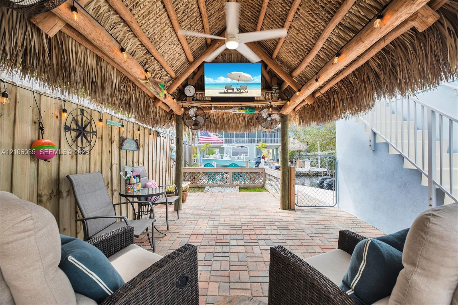 Covered patio featuring a thatched roof, brick paver flooring, ceiling fan, and string lighting