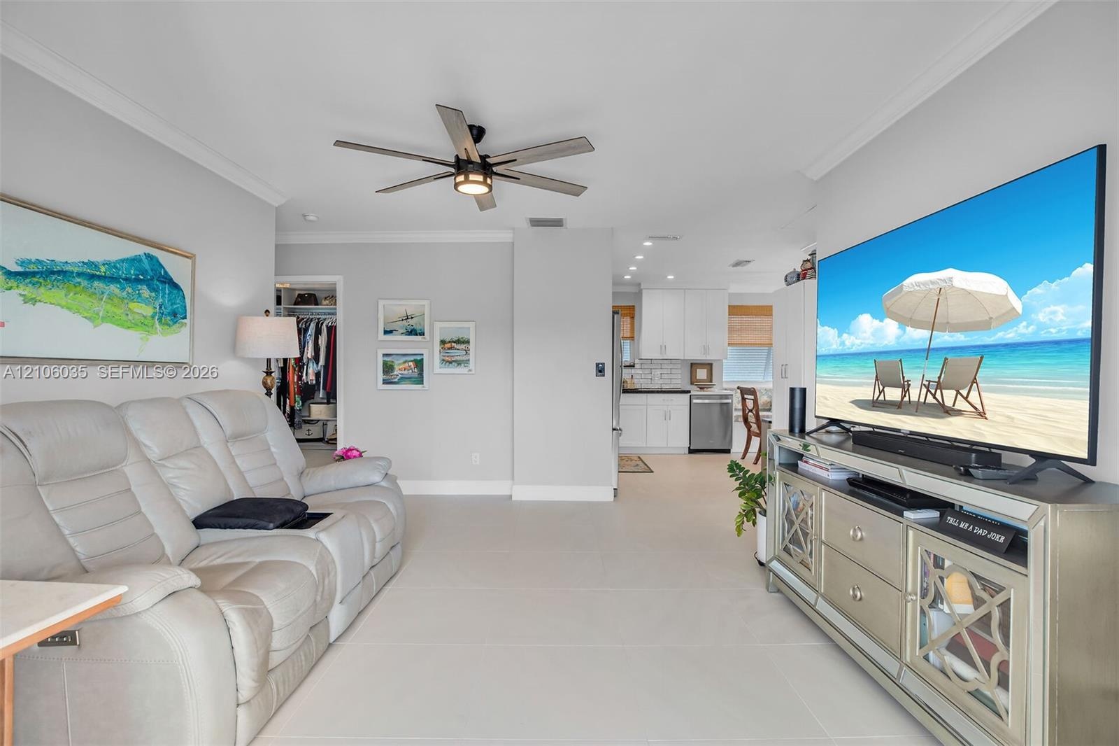 Open living area featuring large-format tile flooring, crown molding, and a modern multi-blade ceiling fan with integrated lighting