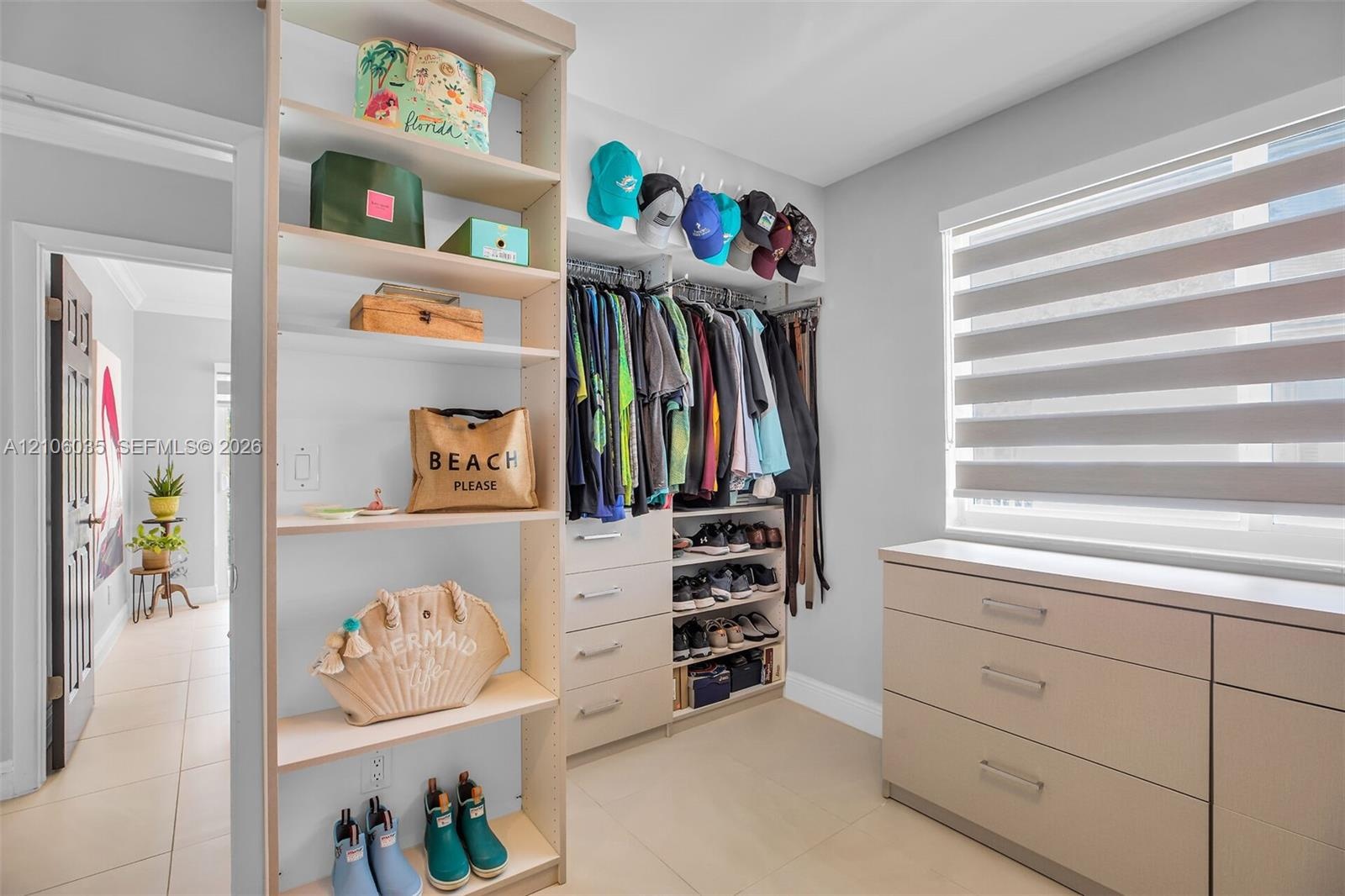 Custom closet organization system featuring light-toned cabinetry, integrated shelving units, tiered storage drawers, and a window fitted with adjusta