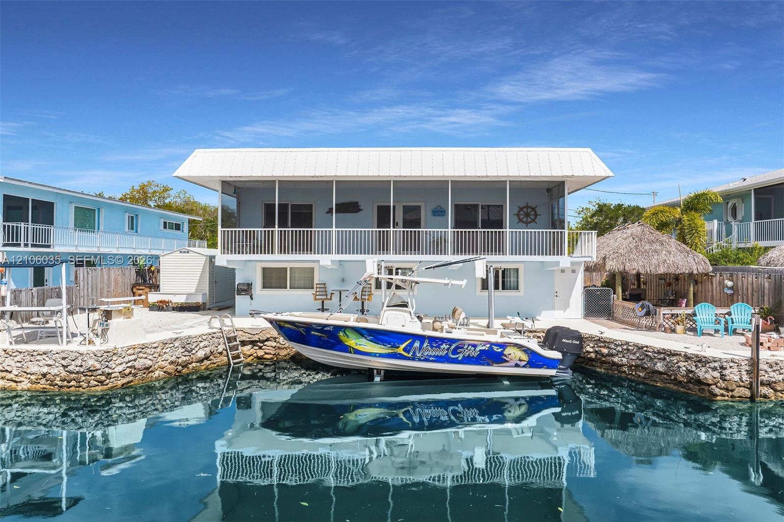 Waterfront residence featuring a private stone-lined seawall, integrated boat slip, elevated screened-in porch, and metal roofing
