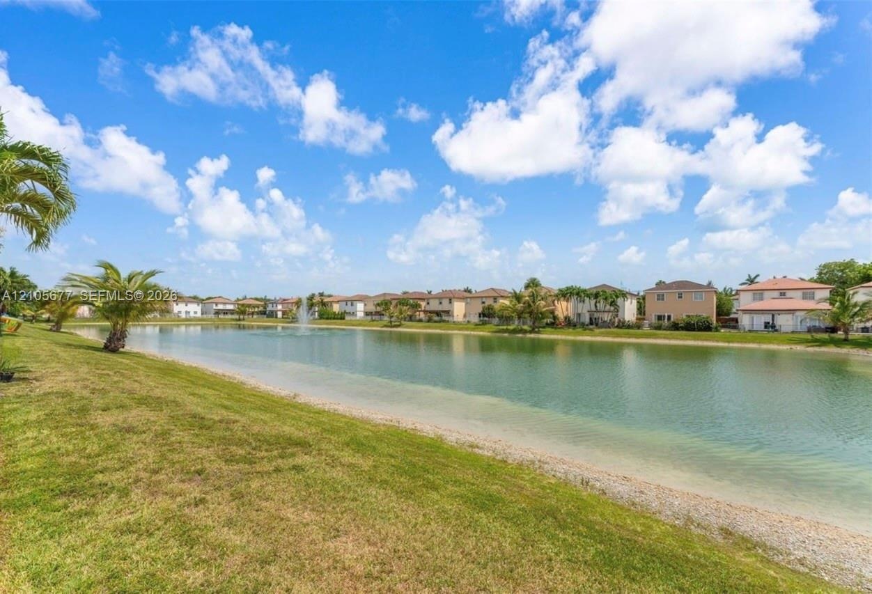 Waterfront grounds featuring a manicured lawn, a central fountain, and mature palm trees