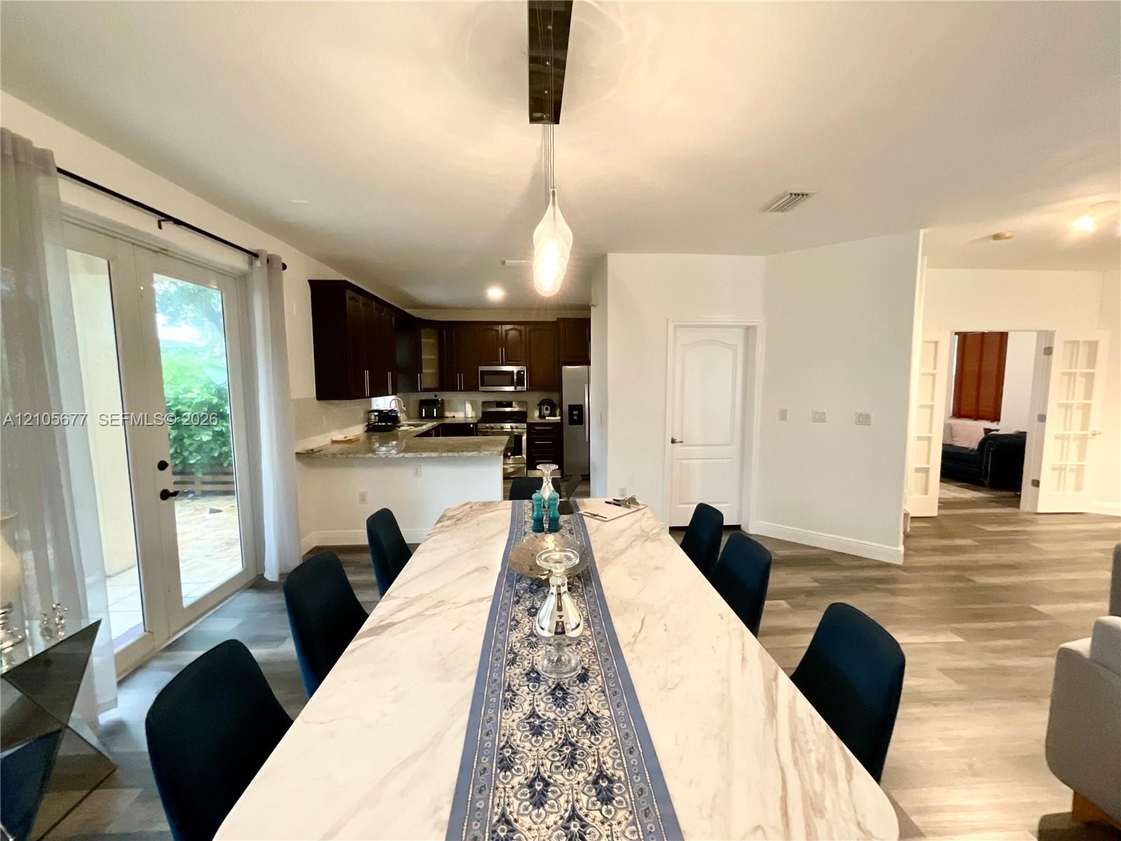 Kitchen featuring dark-toned cabinetry, light-toned stone-surface countertops, and stainless steel appliances, with wood-finish flooring and glass-pan