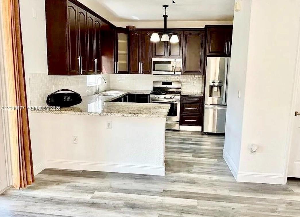 Kitchen featuring dark wood cabinetry, stone-surface countertops, subway tile backsplash, stainless steel appliances, and wood-finish flooring