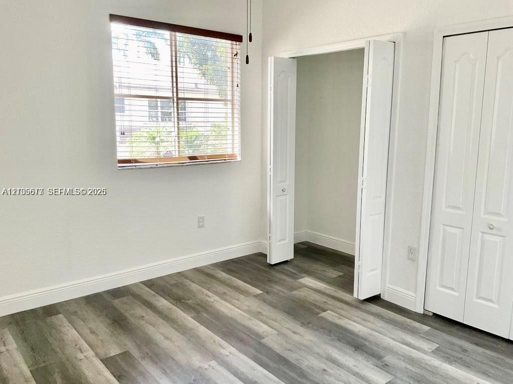 Interior space featuring wood-finish flooring, white walls, horizontal window blinds, and dual bi-fold closet doors