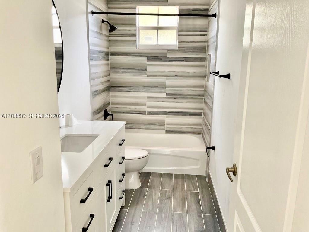 Bathroom featuring a white vanity with a white solid-surface countertop, matte black hardware, horizontal multi-tonal wall tile in the tub enclosure, 