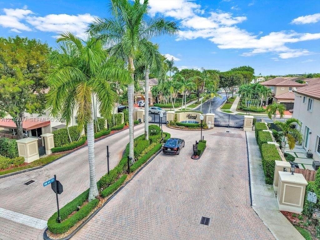 Gated community entrance featuring paver-stone driveways, ornamental stone pillars, professional landscaping with mature palm trees, and structural se