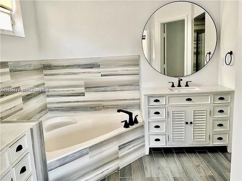 Bathroom featuring a white dual-sink vanity with louvered cabinets, a circular mirror, corner soaking tub, horizontal-patterned wall tiling, and wood-
