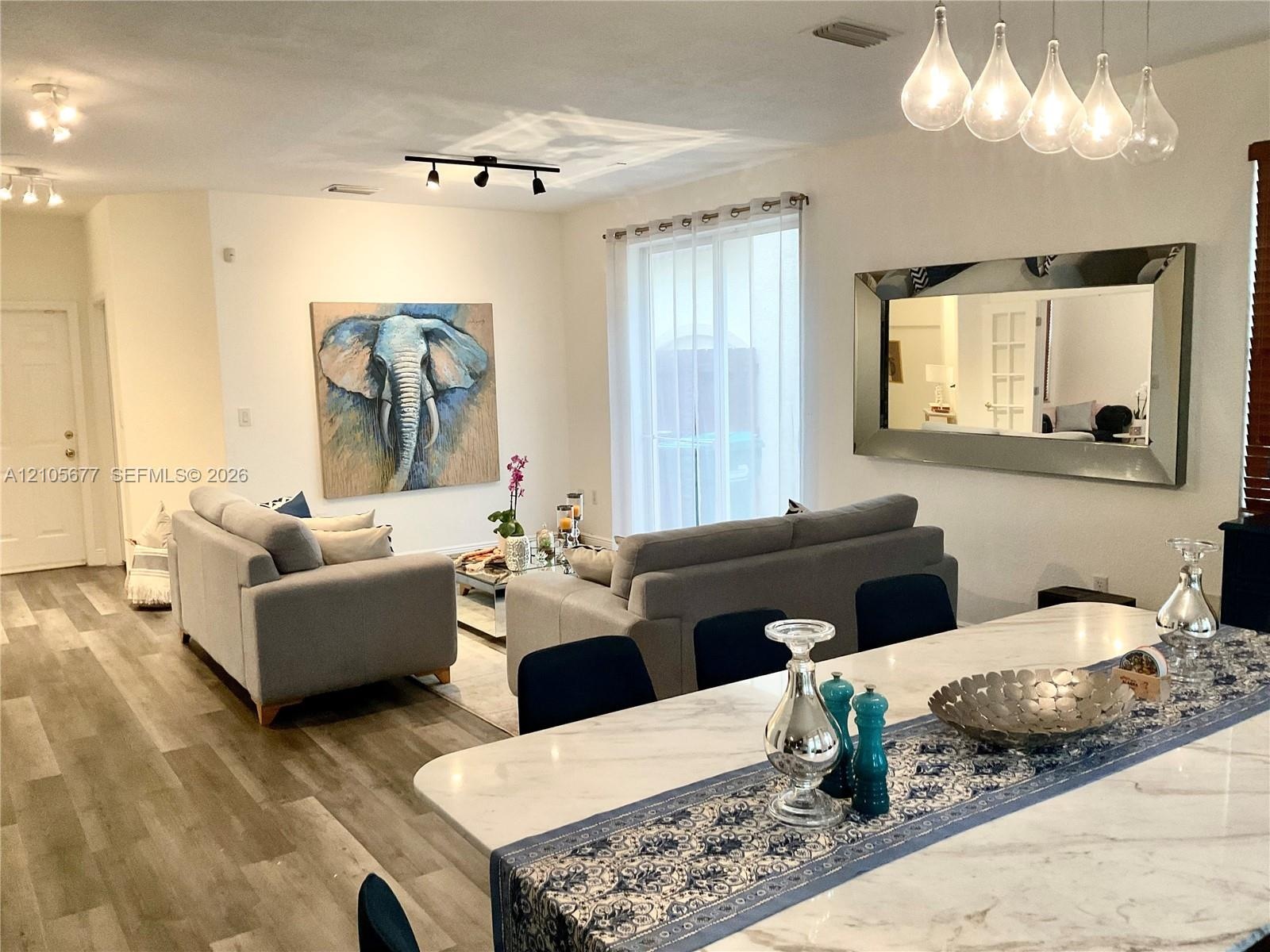Open-concept interior featuring wood-finish flooring, multi-pendant lighting, track lighting, sliding glass door, and a stone-surface kitchen island