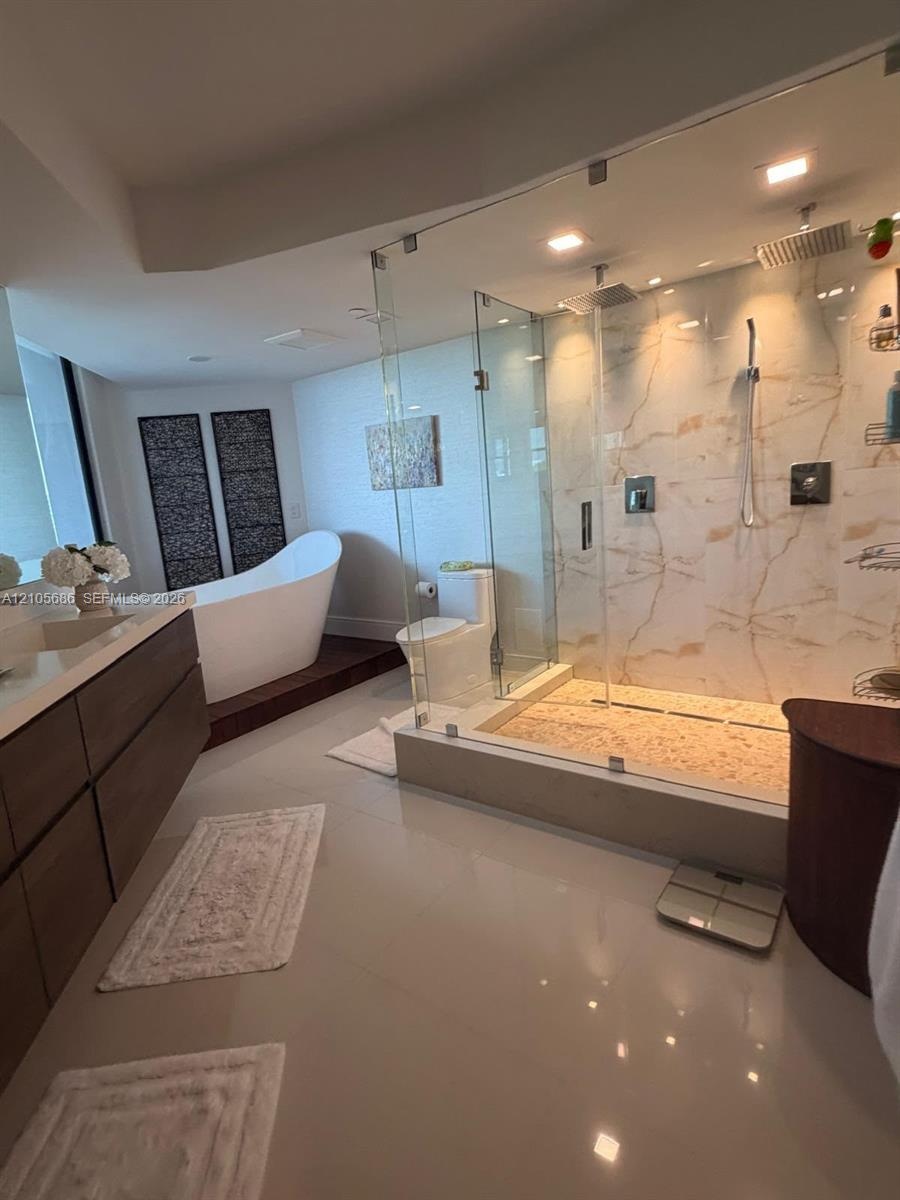 Bathroom featuring a walk-in glass-enclosed shower with large-format stone-patterned wall tile, pebble-texture shower flooring, a freestanding soaking